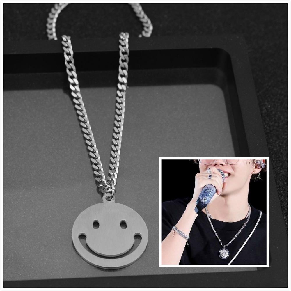 J-Hope 'Sunshine' smiley necklace displayed elegantly on a stylish black tray with a close-up of the pendant and a performer holding a microphone.
